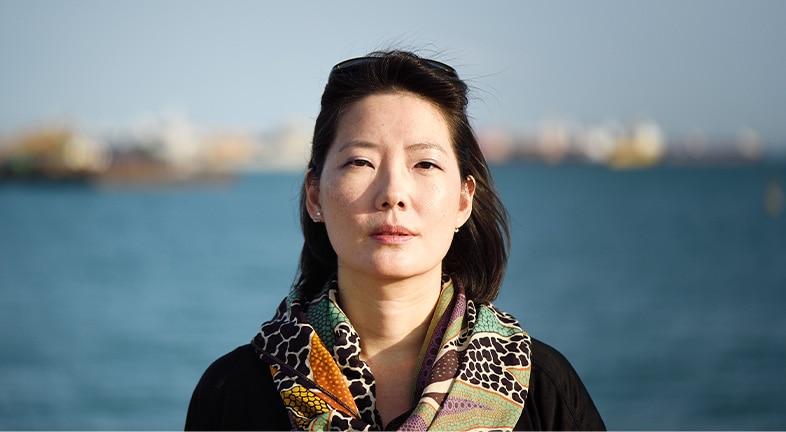 Woman with a full head of hair looking directly at the camera with a body of water in the background.