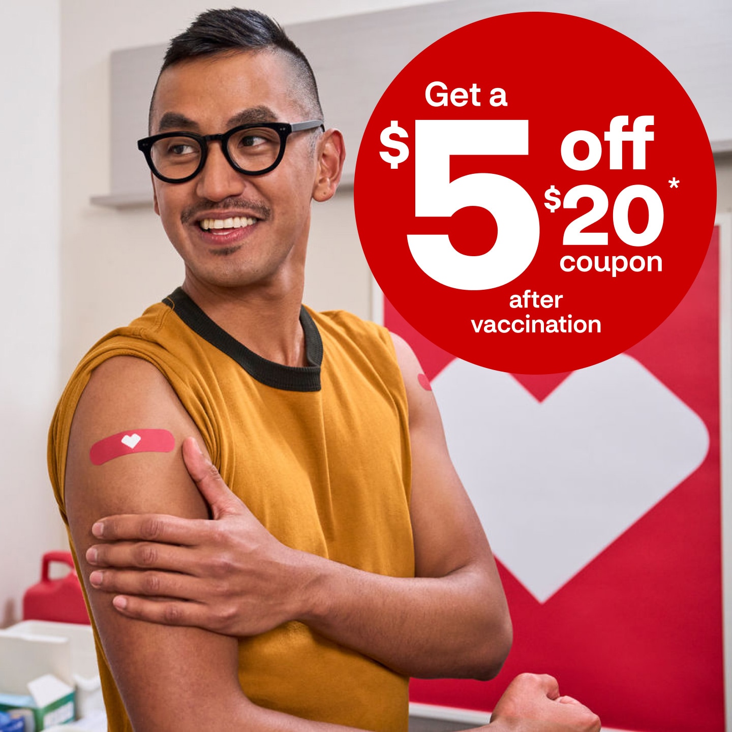 A man smiles and holds his bare right arm that displays a bandage with the CVS heart.