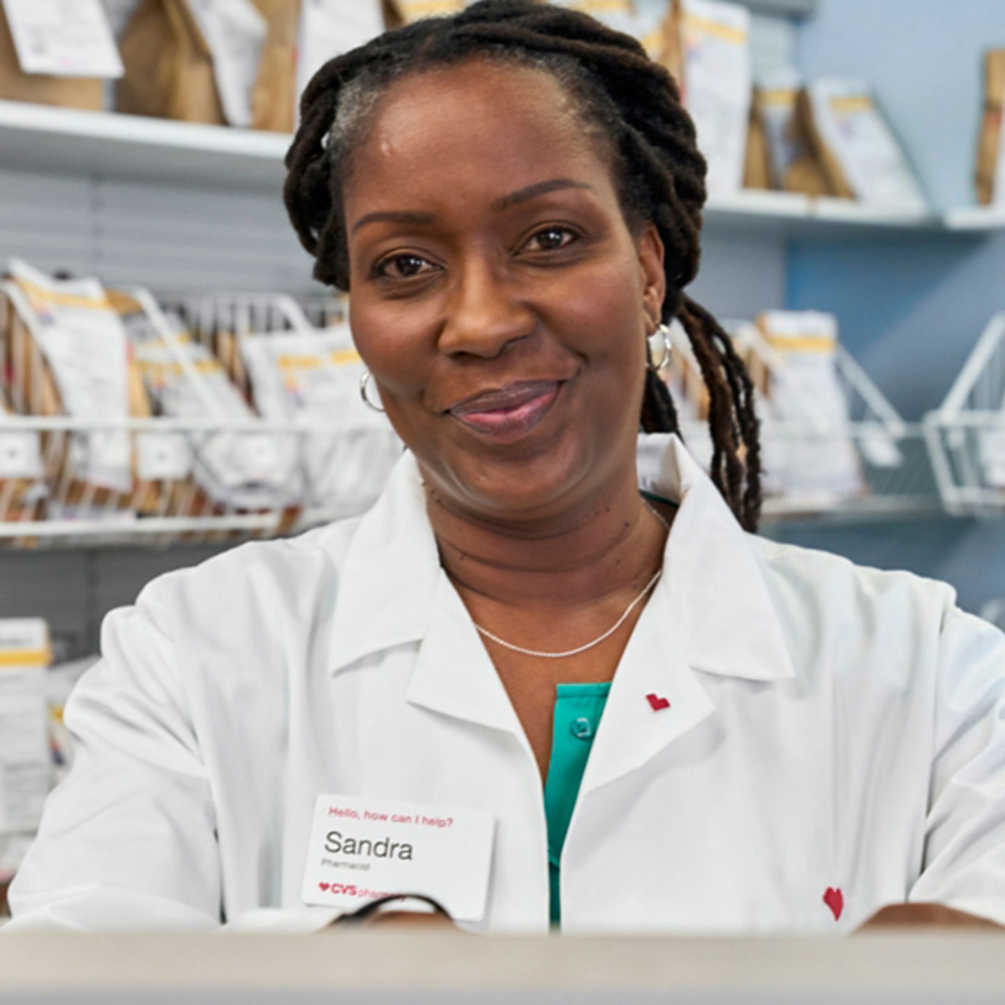 Female pharmacist smiles as she stands in front of a prescription pick-up rack.