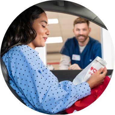 Female customer in car at drive-thru window receiving her prescriptions from pharmacy team member at window