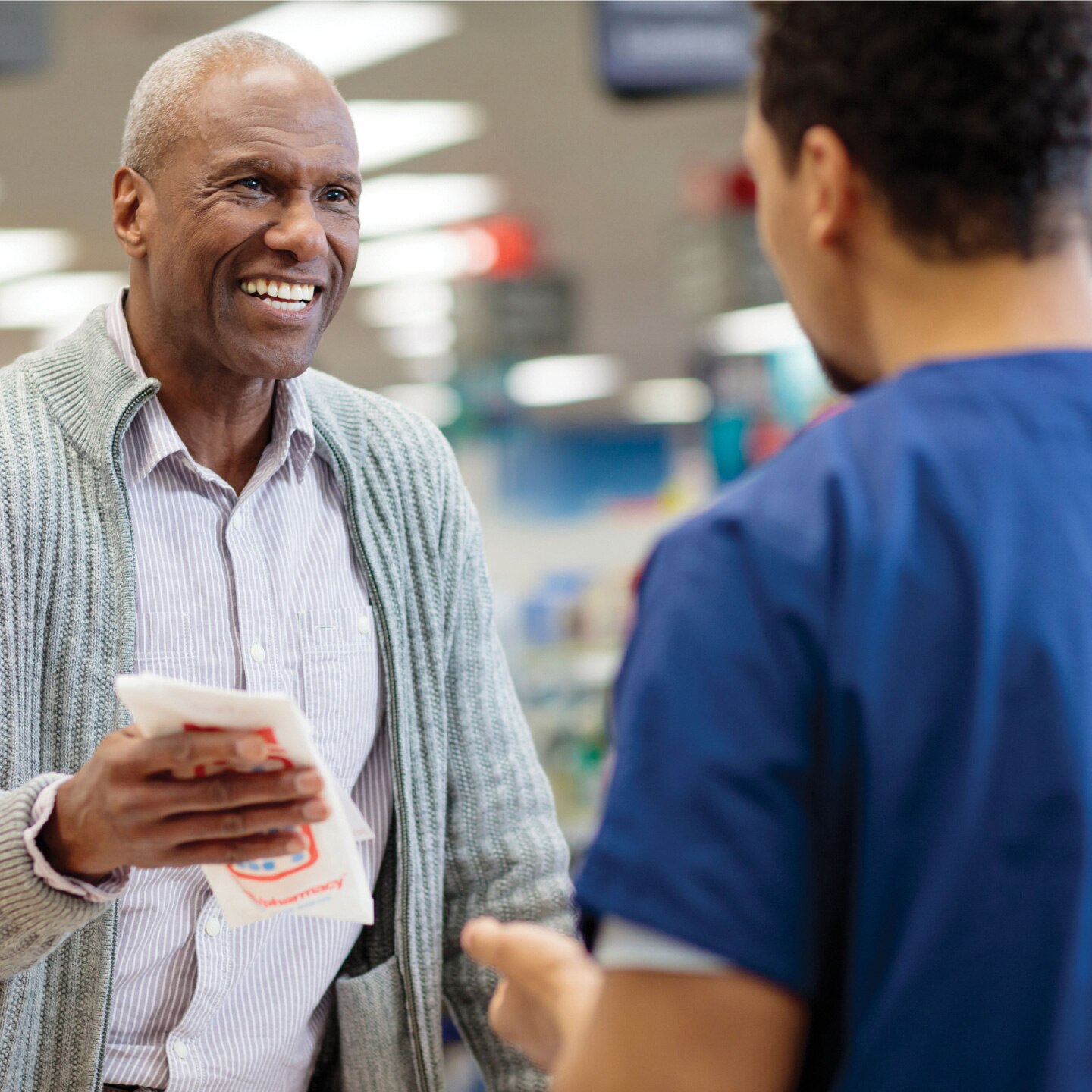 Smiling customer at pharmacy counter holding Rx bag and talking to pharmacist