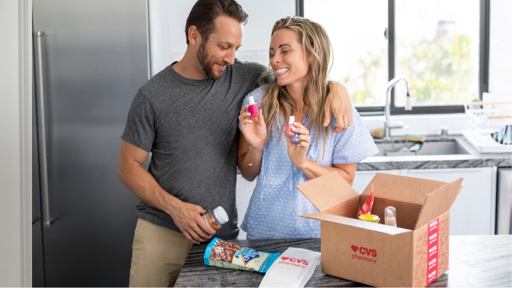 Una pareja sonriente desempaca su entrega de CVS en la cocina.