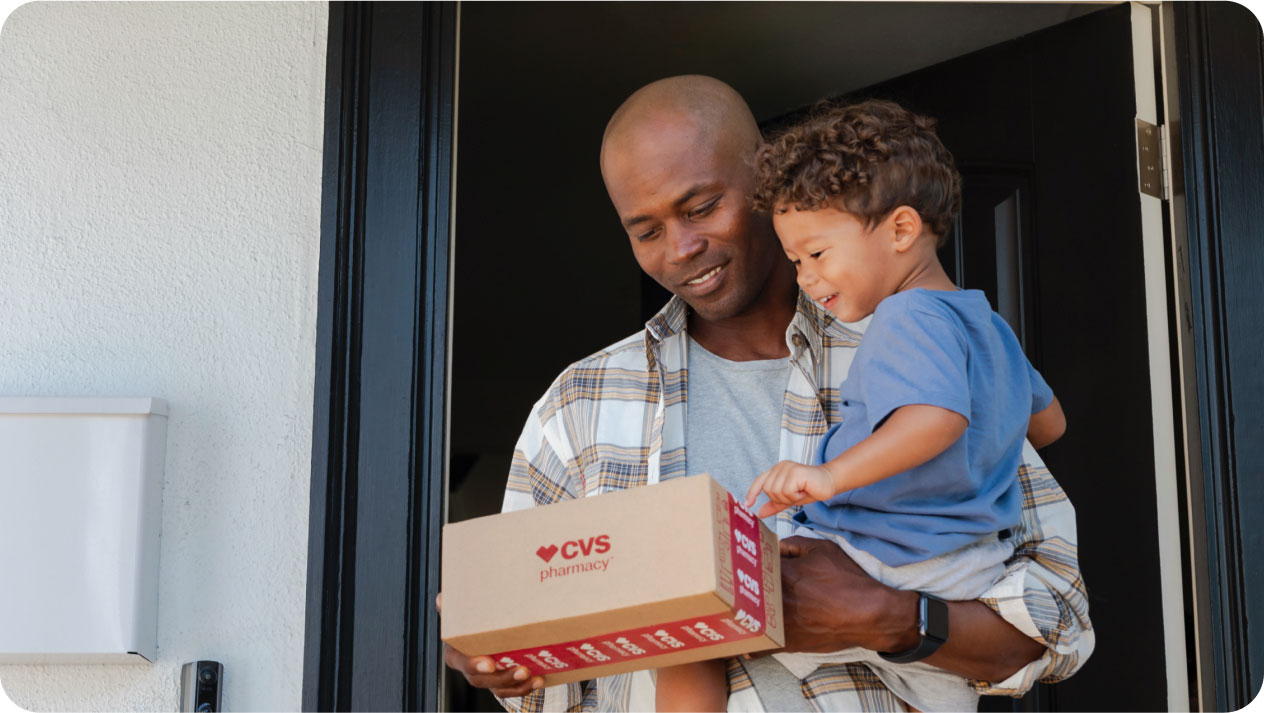 A father holds his son while he brings in his prescription delivery order from CVS pharmacy.